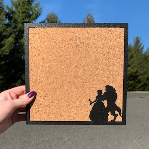 May include: A cork board with a black frame and a silhouette of Belle and the Beast from Beauty and the Beast.