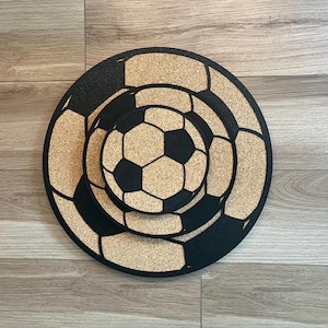 May include: Three cork coasters featuring a black and white football design. The coasters are stacked on top of each other.