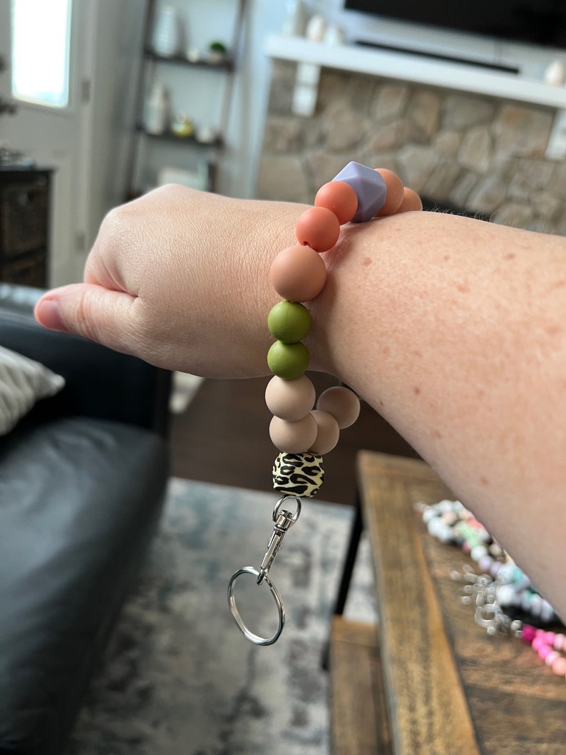 May include: A wristlet keychain with a variety of colorful silicone beads in shades of peach, green, and tan. The keychain includes a leopard print bead and a silver-colored clasp and key ring.