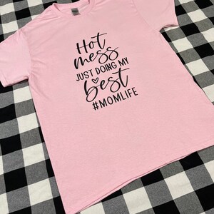 May include: Pink t-shirt with black text that reads "Hot mess just doing my best #momlife".