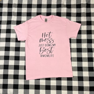 May include: Pink t-shirt with black text that reads "Hot mess just doing my best #momlife".