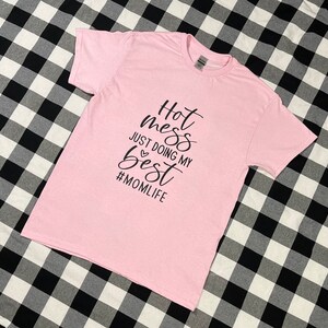May include: Pink t-shirt with black text that reads "Hot mess just doing my best #momlife"