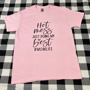 May include: Pink t-shirt with black text that reads "Hot mess just doing my best #momlife".