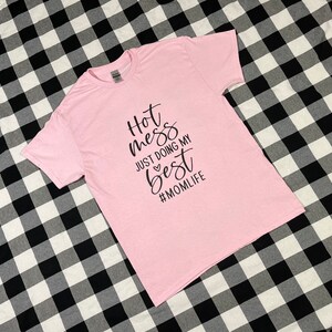 May include: Pink t-shirt with black text that reads "Hot mess just doing my best #momlife".