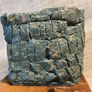 Peut inclure: Un récipient cylindrique en céramique doté d'un émail bleu-vert craquelé et fortement texturé. La surface présente un réseau de fissures profondes et d'écailles irrégulières en relief révélant une base beige clair sous la finition bleu canard.