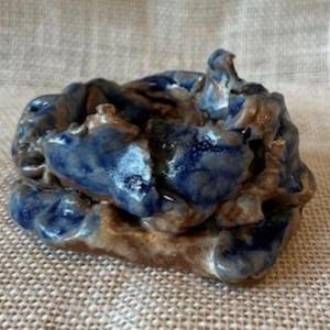 May include: A small, handmade ceramic bowl with a blue and brown glaze. The bowl has an irregular, organic shape and a rough texture.