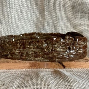 Könnte beinhalten: Ein brauner Keramik-Pflanztopf mit einem strukturierten, wellenförmigen Design. Der Topf steht auf einem Holzsockel.