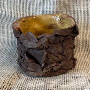 May include: A handmade ceramic bowl with a rough, textured exterior in shades of brown. The interior has a smooth, golden-yellow glaze. The bowl's unique design and earthy tones suggest it could be used for decorative purposes or serving.