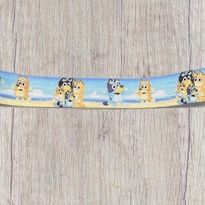 May include: A blue and white elastic headband with a repeating pattern of cartoon dogs on a beach.