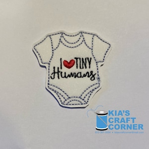 May include: White iron-on patch with a red heart and the text "I love tiny humans" in black embroidery. The patch is shaped like a baby onesie.