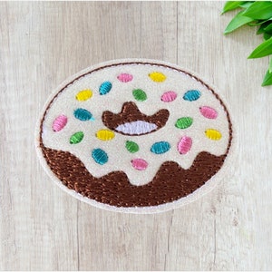 May include: A white donut with brown frosting and colorful sprinkles. The donut has a white frosting design in the center that resembles a cowboy hat.