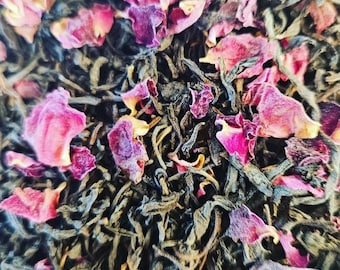 May include: Close-up image of loose leaf tea with dried pink rose petals. The tea leaves are dark green and mixed with the vibrant pink petals. The macro shot highlights the texture and colour of the tea.