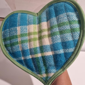 May include: Heart-shaped quilted pot holder with a blue, green, and white plaid pattern. The pot holder has a green border. A charming addition to any kitchen.