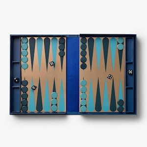 May include: A backgammon board game set featuring a tan playing surface with dark blue and light blue triangular points. The set includes dark blue and light blue circular checkers, four black dice, and one black doubling cube with white numbers.