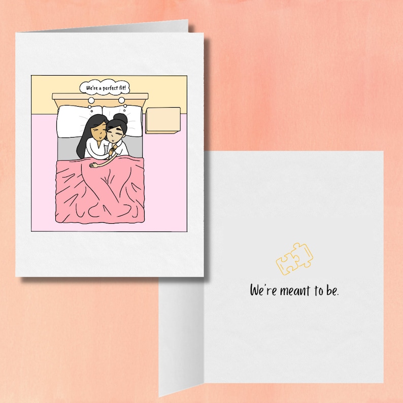 May include: A greeting card with a cartoon illustration of two people in bed together. The card reads "We're a perfect fit!" and the inside reads "We're meant to be." with a puzzle piece icon.