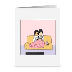 K&ouml;nnte beinhalten: Zwei Personen sitzen auf einem gelben Sofa unter einer rosa Decke und schauen fern. Beide halten Sch&uuml;sseln und L&ouml;ffel in der Hand, und neben ihnen steht ein Glas auf dem Sofa.
