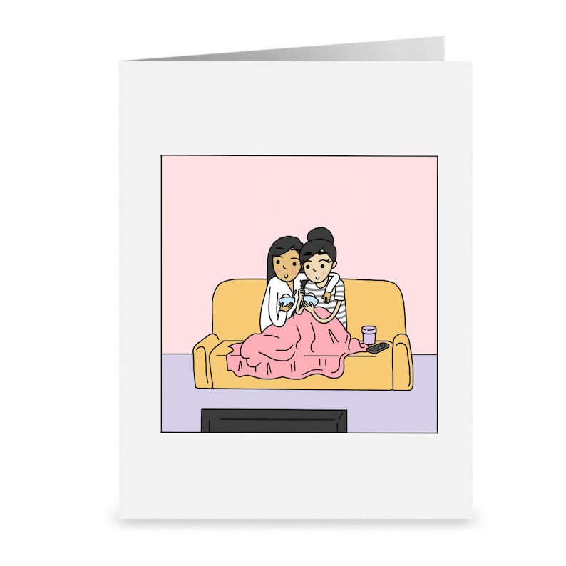 K&ouml;nnte beinhalten: Zwei Personen sitzen auf einem gelben Sofa unter einer rosa Decke und schauen fern. Beide halten Sch&uuml;sseln und L&ouml;ffel in der Hand, und neben ihnen steht ein Glas auf dem Sofa.