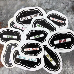 May include: A collection of white cloud-shaped stickers with black backgrounds and colourful text. The text on the stickers reads "SUS", "NOT SUS!" and "ISNS".