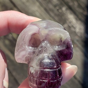 May include: A purple and white fluorite crystal skull. The skull is carved in detail and has a smooth, polished finish.