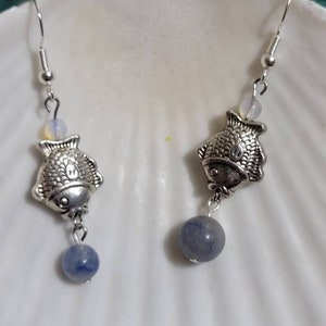 May include: A pair of silver fish earrings with blue gemstone beads. The fish are detailed with scales and have a silver hook.