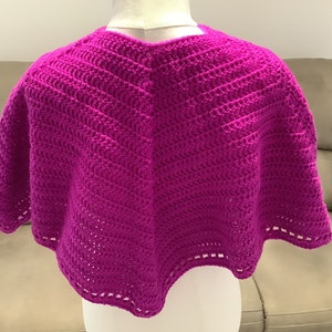 Può includere: Uno scialle all'uncinetto di colore magenta brillante con un bordo a festoni.