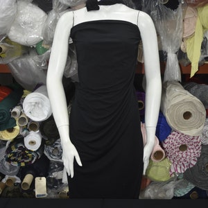 May include: A black strapless dress on a white mannequin, surrounded by rolls of fabric in various colors and patterns.