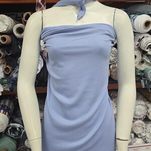 Puede incluir: Un vestido tubo sin tirantes de color azul claro, confeccionado en tejido acanalado el&aacute;stico. La prenda incluye un pa&ntilde;uelo de cuello a juego de tejido acanalado azul claro anudado en la parte delantera, creando un conjunto coordinado en un maniqu&iacute;.