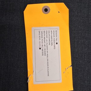 May include: An orange tag with a hole at the top, attached to a dark gray fabric. The tag contains white text with details about the fabric's composition, including 46% polyester, 36% wool, and 14% nylon. The fabric width is 46 inches.
