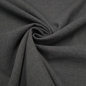 May include: Dark gray fabric with a subtle texture, draped and folded to create soft curves and shadows. The fabric's color appears consistent throughout, with a slight sheen visible in the folds. The material is likely suitable for apparel or home decor.