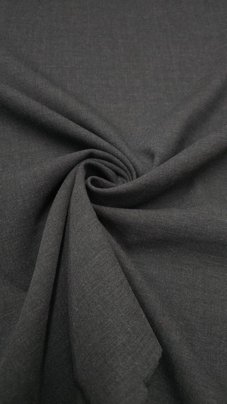 May include: Dark gray fabric with a subtle texture, draped and folded to create soft curves and shadows. The fabric's color appears consistent throughout, with a slight sheen visible in the folds. The material is likely suitable for apparel or home decor.