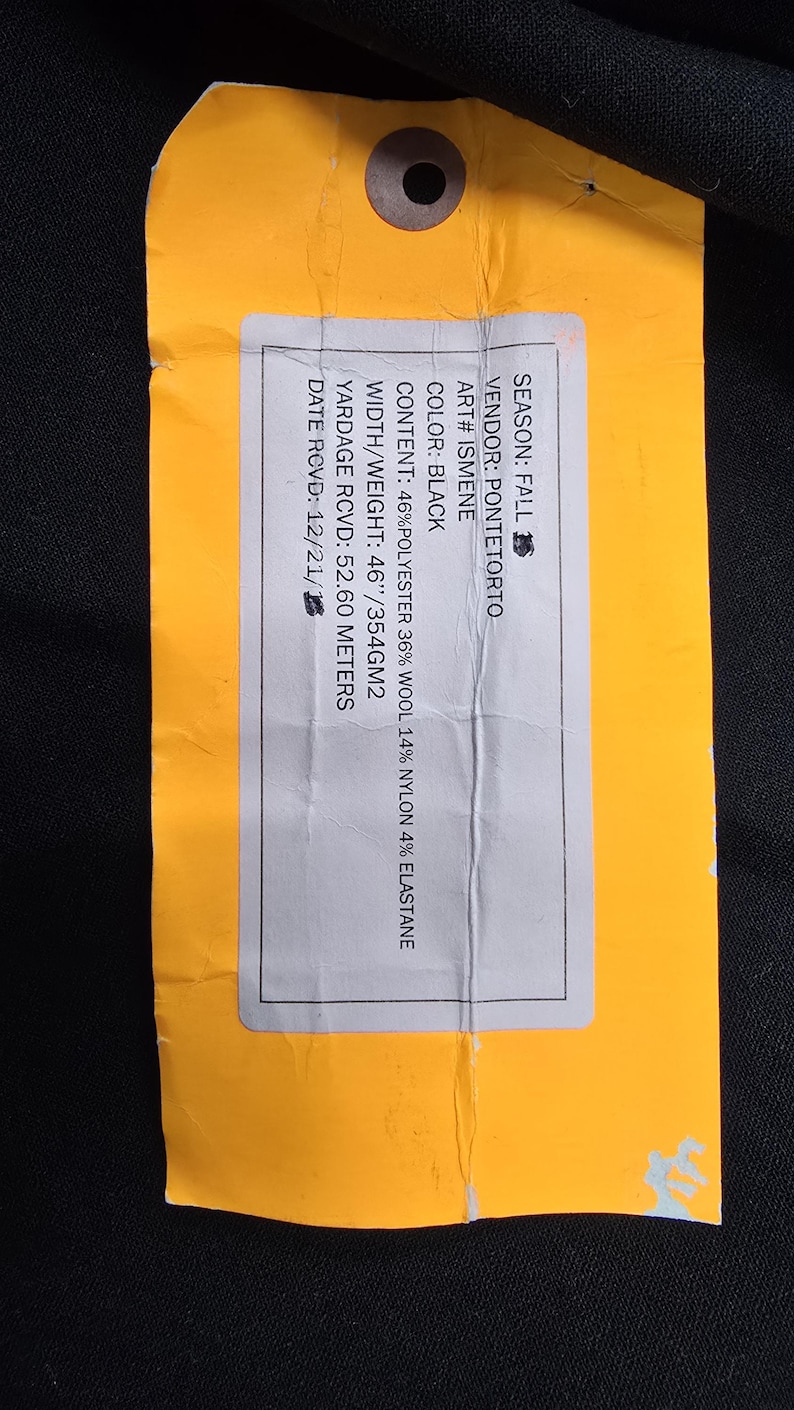 May include: A yellow tag with a hole at the top, featuring text about fabric content and specifications. The tag includes details such as the vendor, color (black), and material composition: 46% polyester, 36% wool, 14% nylon, and 4% elastane.