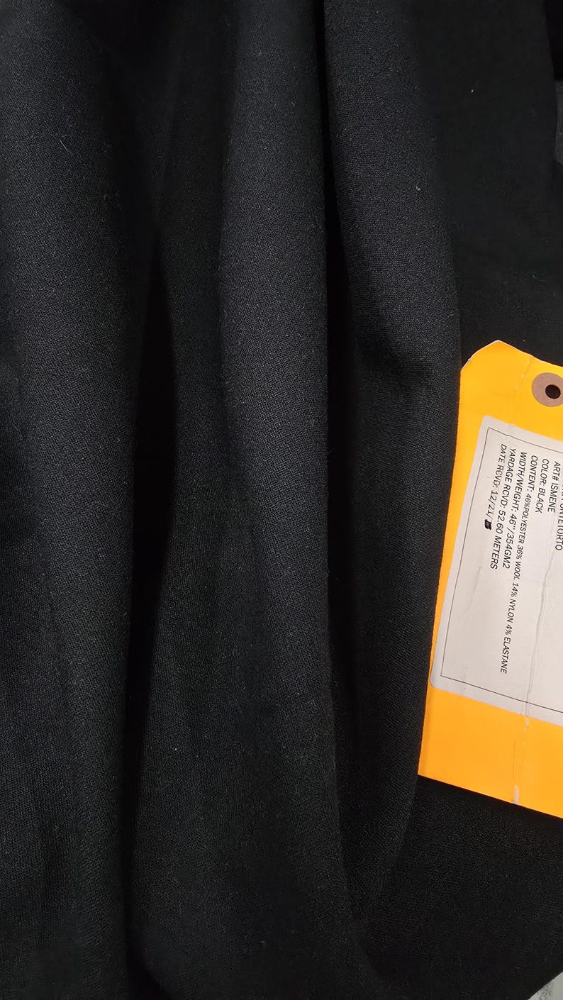 May include: Black fabric with a tag attached. The tag provides details about the fabric's composition, including 46% polyester, 36% wool, 14% nylon, and 4% elastane. The fabric width is 46 inches, and the weight is 354 grams per square meter.