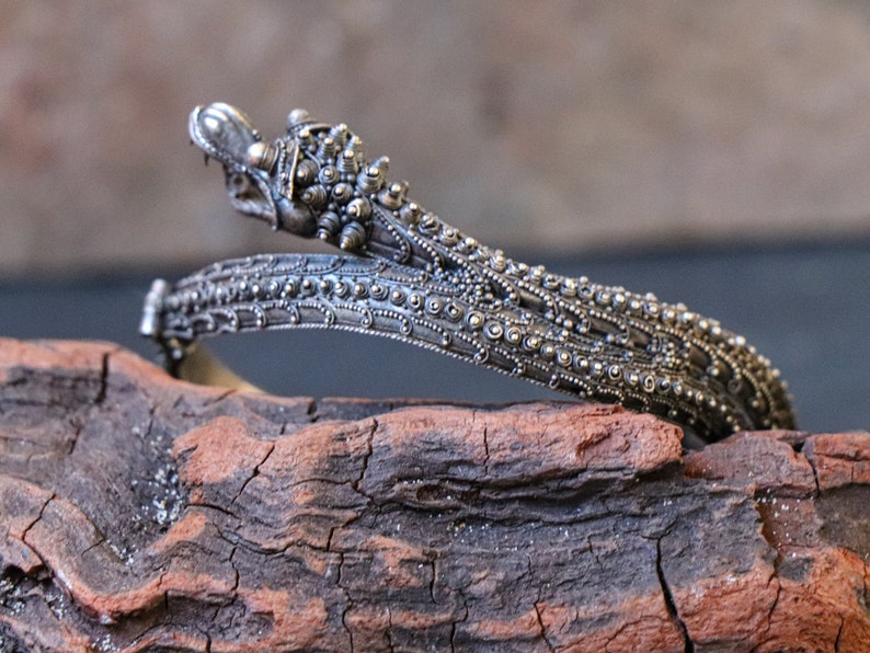 Pu&ograve; includere: Un braccialetto d'argento con dettagli intricati, che presenta un design a testa di drago. Il braccialetto &egrave; realizzato in argento e ha una superficie testurizzata.
