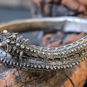Pu&ograve; includere: Un braccialetto d'argento con dettagli intricati, che presenta una testa di drago con un motivo a perline.