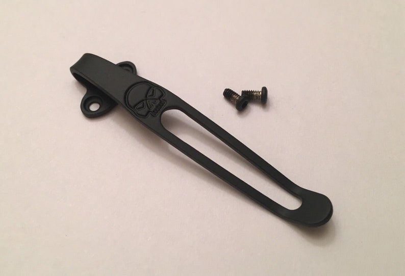 Puede incluir: Clip de bolsillo de titanio negro con un dise&ntilde;o de calavera y dos peque&ntilde;os tornillos negros.