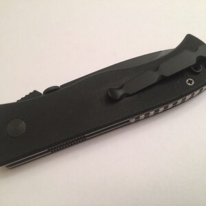 May include: Black folding knife with a black pocket clip and a textured black handle.