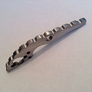 May include: A silver metal tool with a serrated edge and a hole in the center. The tool is designed for opening packages and other tasks.