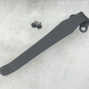 Puede incluir: Un clip de bolsillo de metal negro con dos pequeños tornillos plateados.