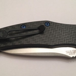 Puede incluir: Un cuchillo de bolsillo negro con un mango de fibra de carbono y una hoja plateada. El cuchillo tiene un logotipo de calavera en el clip y un bot&oacute;n plateado en la parte posterior. La hoja est&aacute; parcialmente abierta y el texto "GT20CF" y "EAR-PENNED MADE IN USA" son visibles en la hoja.