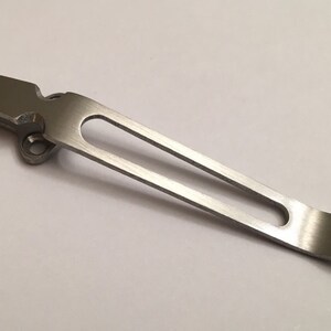 May include: A silver metal pocket clip with a rounded end and a small hole near the top.