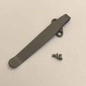 May include: A gray metal pocket clip with two small screws. The clip is designed to attach to a pocket or belt.