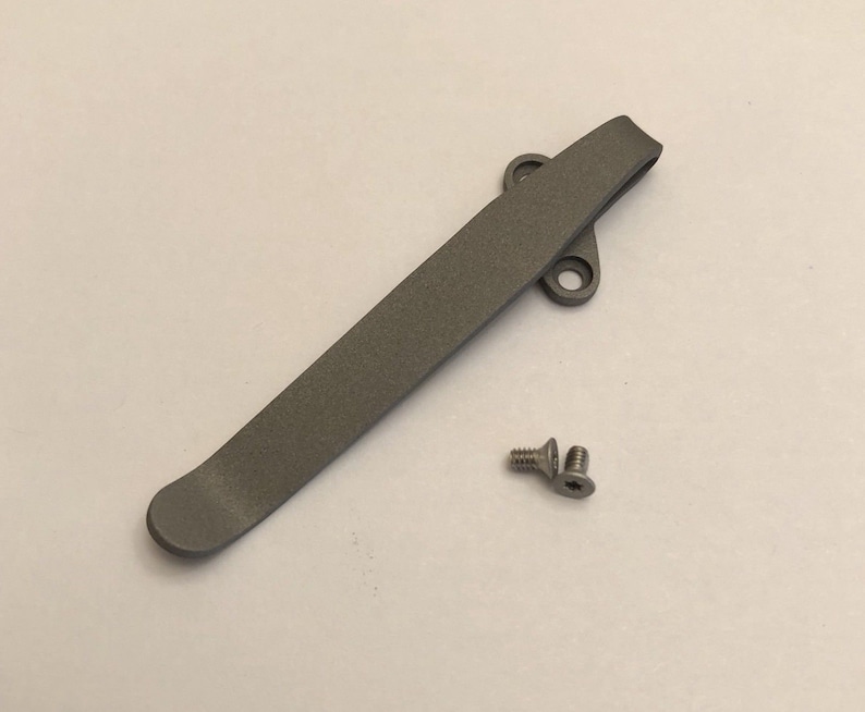 May include: A gray metal pocket clip with two small screws. The clip is designed to attach to a pocket or belt.