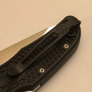 May include: Black pocket knife with a textured black handle and a black pocket clip. The pocket clip has a spider logo on it.