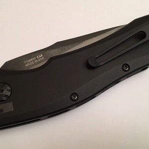 May include: Black folding knife with a pocket clip and the text "71008W  CAI MADE IN USA" engraved on the side.
