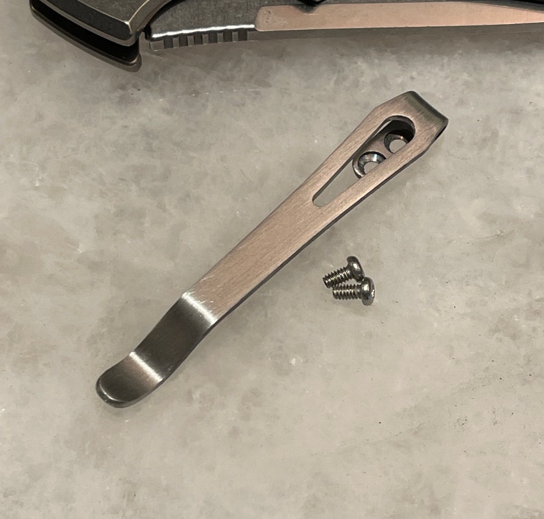 May include: A silver pocket clip for a knife with two screws.