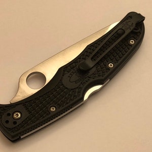 May include: A black and silver pocket knife with a textured black handle and a clip. The knife has a Spyderco logo on the handle.