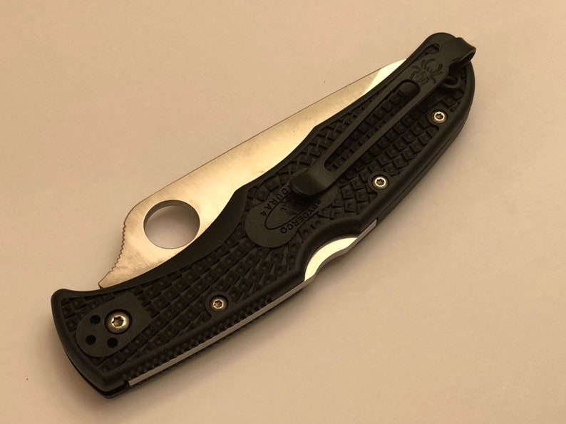 May include: A black and silver pocket knife with a textured black handle and a clip. The knife has a Spyderco logo on the handle.