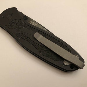 May include: Black pocket knife with a textured handle and a silver pocket clip. The knife has the text "1070TSBW" and "CR  Premium" engraved on the handle.