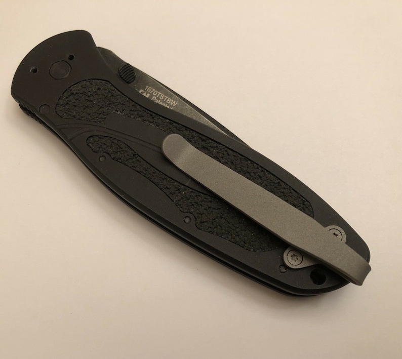 May include: Black pocket knife with a textured handle and a silver pocket clip. The knife has the text "1070TSBW" and "CR  Premium" engraved on the handle.