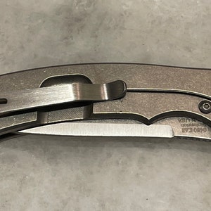 May include: A silver pocket knife with a black handle and a clip. The knife has a partially open blade and the text "GSO  EAF" is visible on the blade.